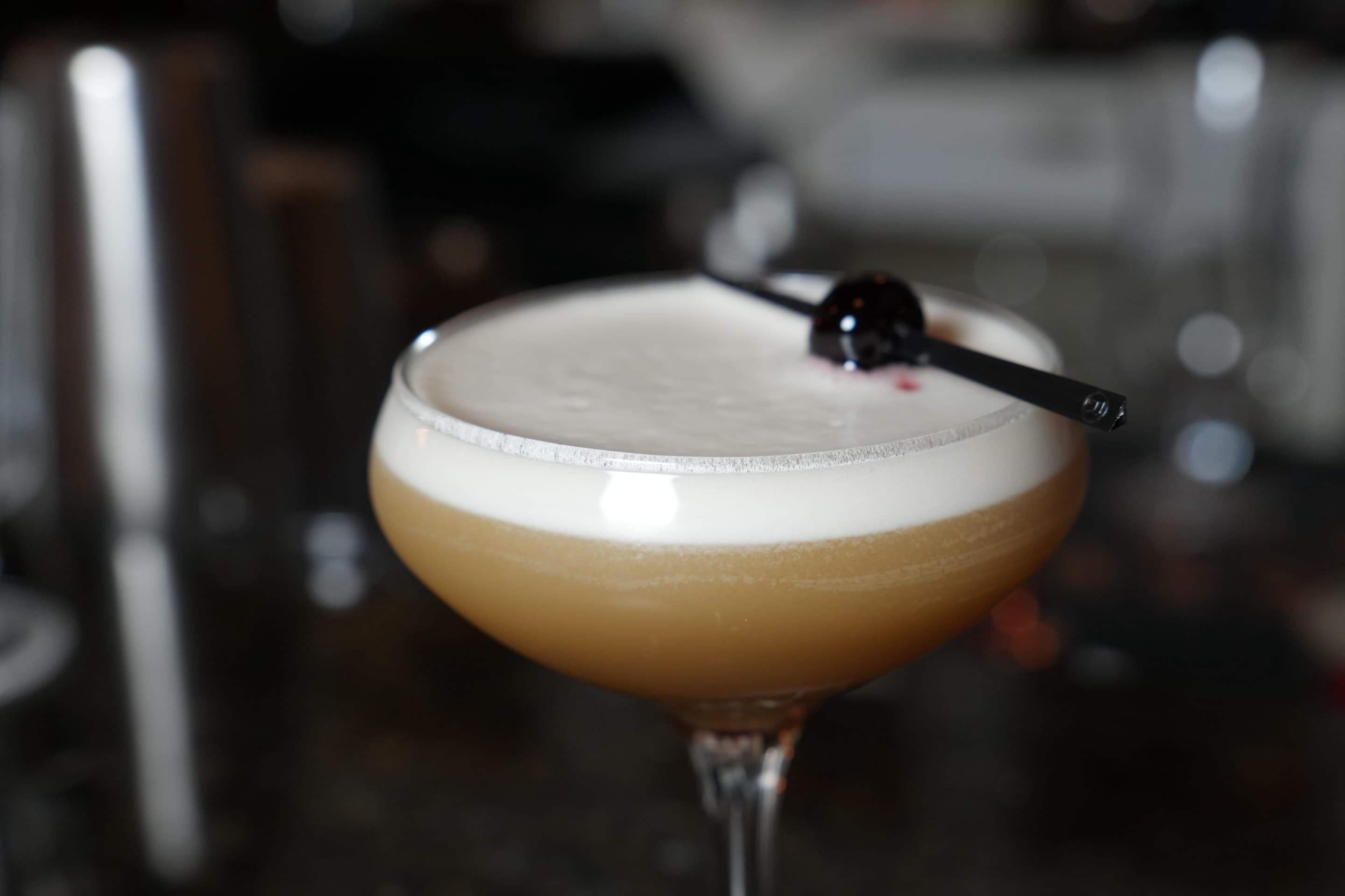 A hand cradling a cocktail on a polished black marble bar, warm bokeh in the background